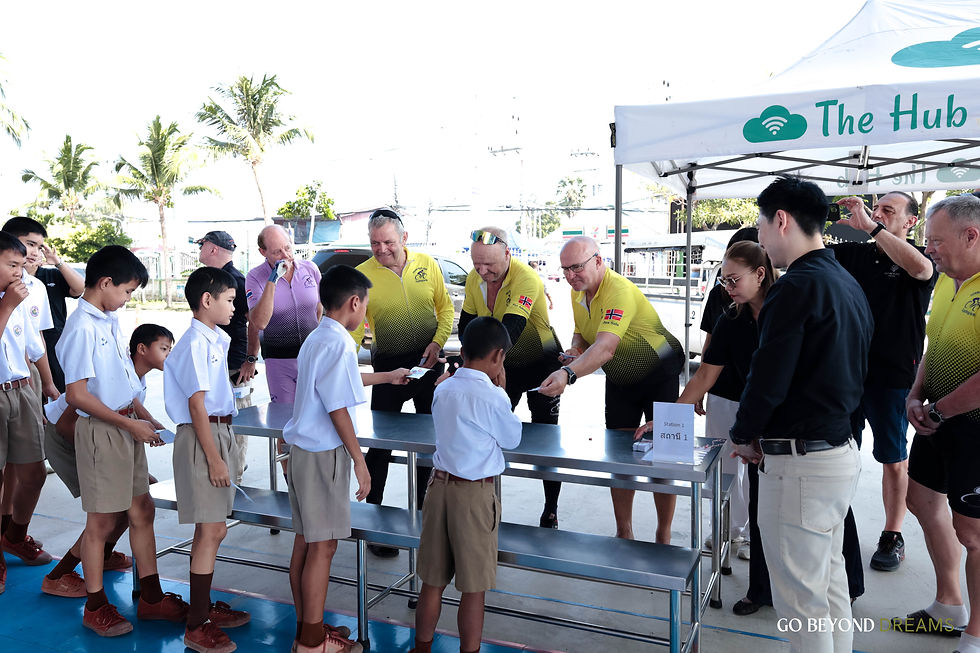 Schoolboys in uniforms receive cards from adults at a table under The Hub tent.
