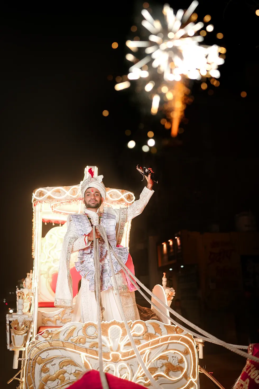 Groom arriving in a decorated baraat carriage with fireworks at an Indian wedding procession