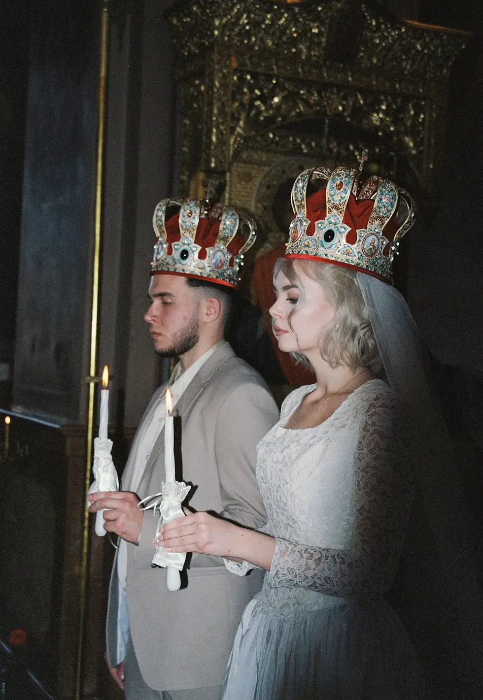 Bride and groom wearing traditional Orthodox wedding crowns and holding candles during a Russian Orthodox marriage ceremony