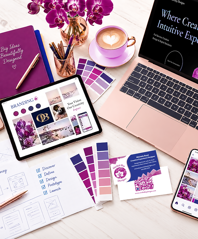 A white wooden desk with branding materials, branded color palettes, company business cards, purpe orchids, a mug of coffee with heart foam, and an orchid-colored notebook with gold lettering that says, "Big Ideas, Beatifully Designed".