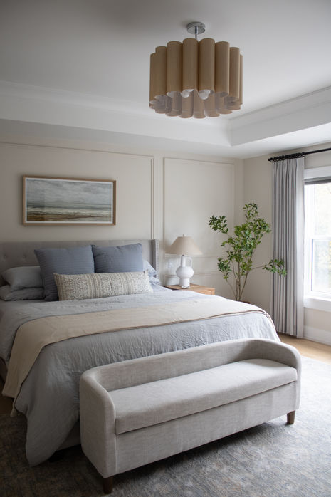 a grey ottoman sits at the end of a bed as part of a classic bedroom design