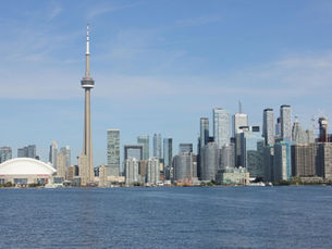 Toronto skyline with CN Tower and Rogers Centre against a clear blue sky, viewed from across the water, creating a calm urban scene.