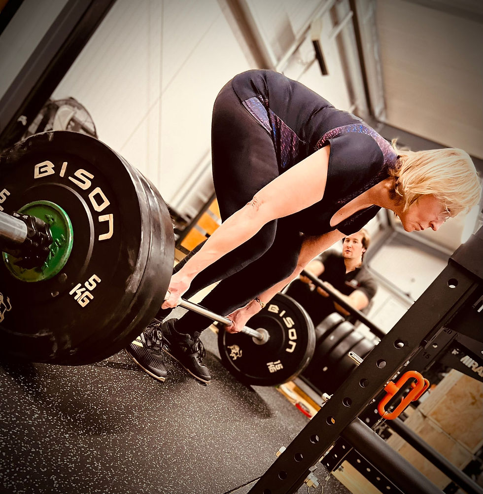 Older adult strength training - 76-year-old woman preparing to deadlift with coaching support, demonstrating safe barbell exercise for longevity and fitness.
