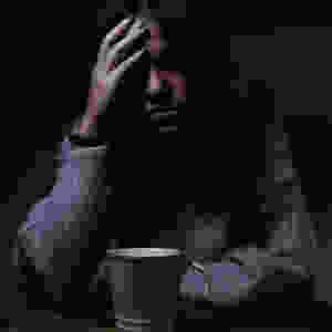 stressed woman with hand on her forehead and cup of coffee in front of her