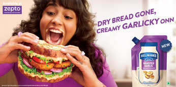 Hellmann's Roasted Garlic vegan mayonnaise advertising photo of a person joyfully biting a loaded sandwich, Zepto delivery badge