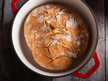 Rustic golden-brown artisan bread baked in a red Dutch oven—demonstrating why Dutch ovens are a baker’s favorite.
