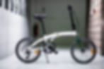 Compact white folding bike indoors against a wall.