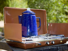Retro-style camping stove with blue enamel coffee pot outdoors, representing sustainable outdoor cooking gear.