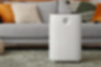Large white air purifier in front of a cozy grey couch with plush pillows and textured rug