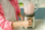 Person wearing a pink jacket using a stainless steel blender to make a strawberry smoothie — close-up shot showing clean, safe kitchen prep with a BPA-free container.