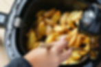 Crispy potato wedges in a family-size air fryer basket, freshly cooked and stirred by hand.