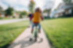Child learning to ride a green bike with training wheels in the neighborhood.