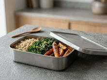 Rectangular stainless steel food container with quinoa, greens, and roasted vegetables on a kitchen counter
