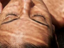 Close-up of a woman’s face with eyes closed under dappled sunlight patterns on the skin