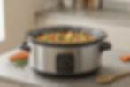 Stainless steel slow cooker simmering vegetable stew on a kitchen countertop