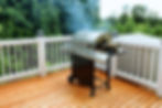 Large outdoor gas grill with multiple burners on a wooden deck patio.