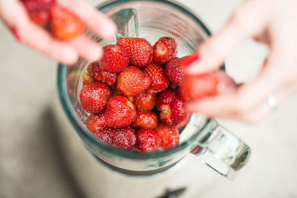 Close-up of hands placing fresh strawberries into a glass blender jar — highlighting clean food prep and plastic-free blending.