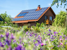 Modern home with solar panels on a red tile roof surrounded by a flowering garden, representing eco-conscious residential solar adoption in 2025