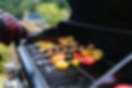 Compact propane gas grill with food trays and vegetables cooking outdoors.