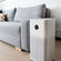 Compact air purifier with clean design placed beside a grey sofa in a modern living room setting