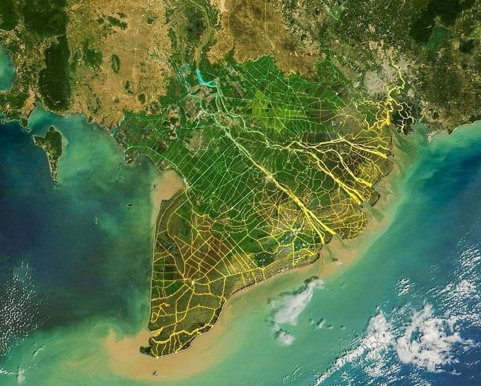Satellite view of land with glowing yellow networks over green and brown terrain by the sea. Blue and turquoise water surrounds the area.