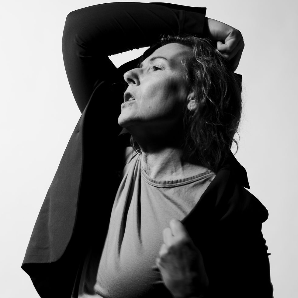 Black and white image of a woman, looking up and to the right, her right arm raised, bent at the elbow, with forearm/hand resting on head.