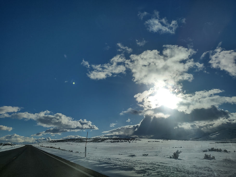 Highway in Nevada with snow-covered fields and a blue sky with sun shining through a cluster of clouds