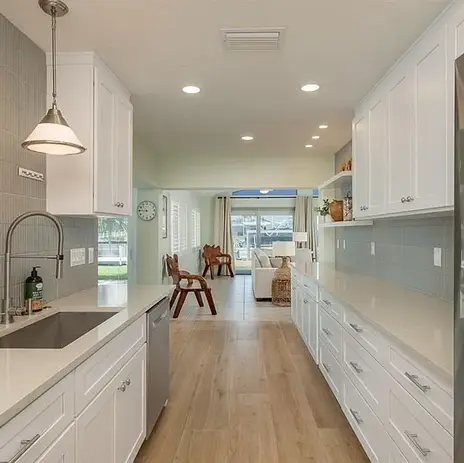 Galley-style kitchen with white shaker cabinets, light wood flooring, vertical sage green tile backsplash, and open display shelving, remodeled by Moll & Co. | Vista in Tampa, FL