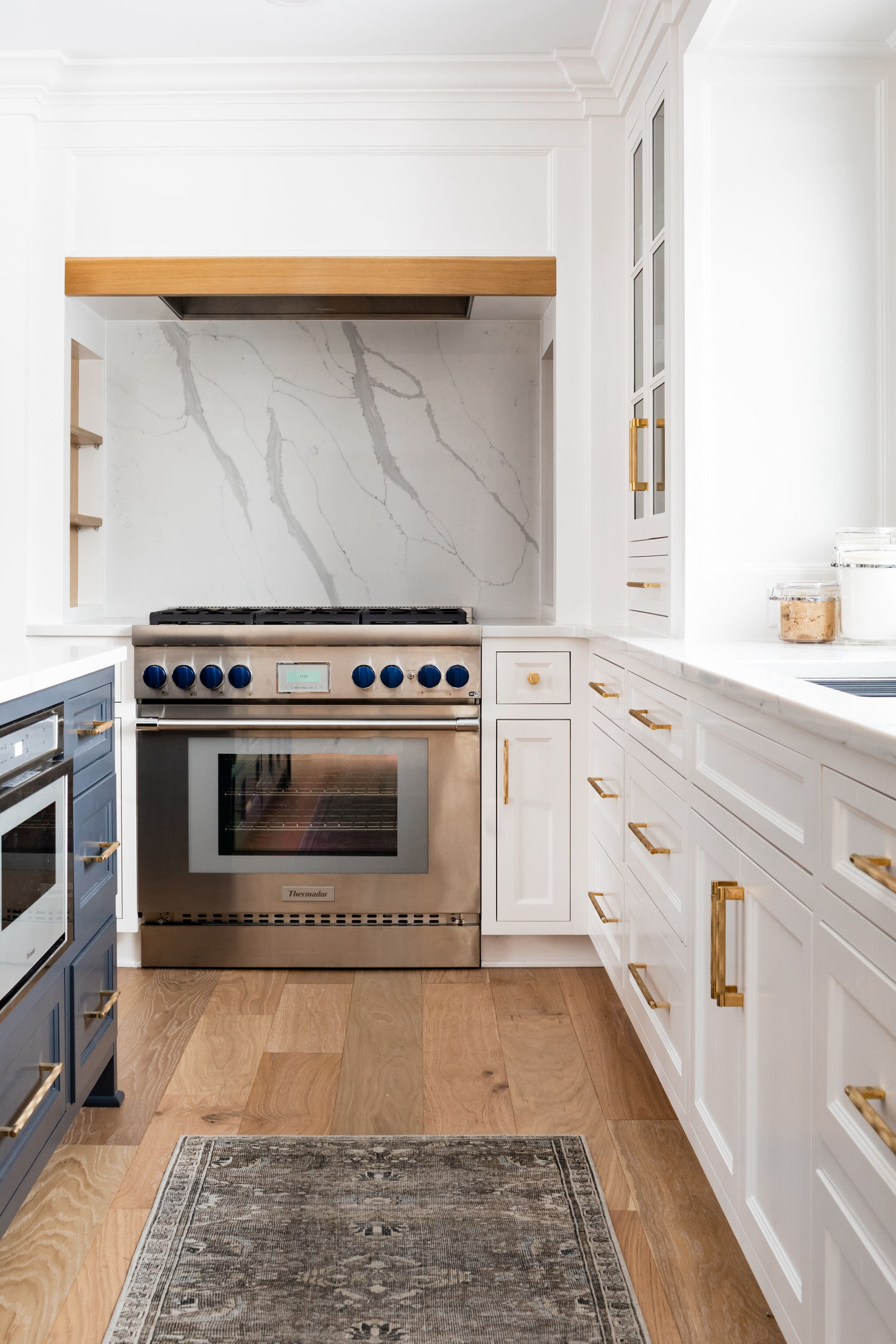 Edina Minnesota custom home interior remodel featuring custom white painted cabinets, Sherwin Williams cyberspace painted island, gold hardware, custom lighting, luxury cabinets, black bar stools, Andersen black windows, Delta faucet, Thermador kitchen range, and white oak accents