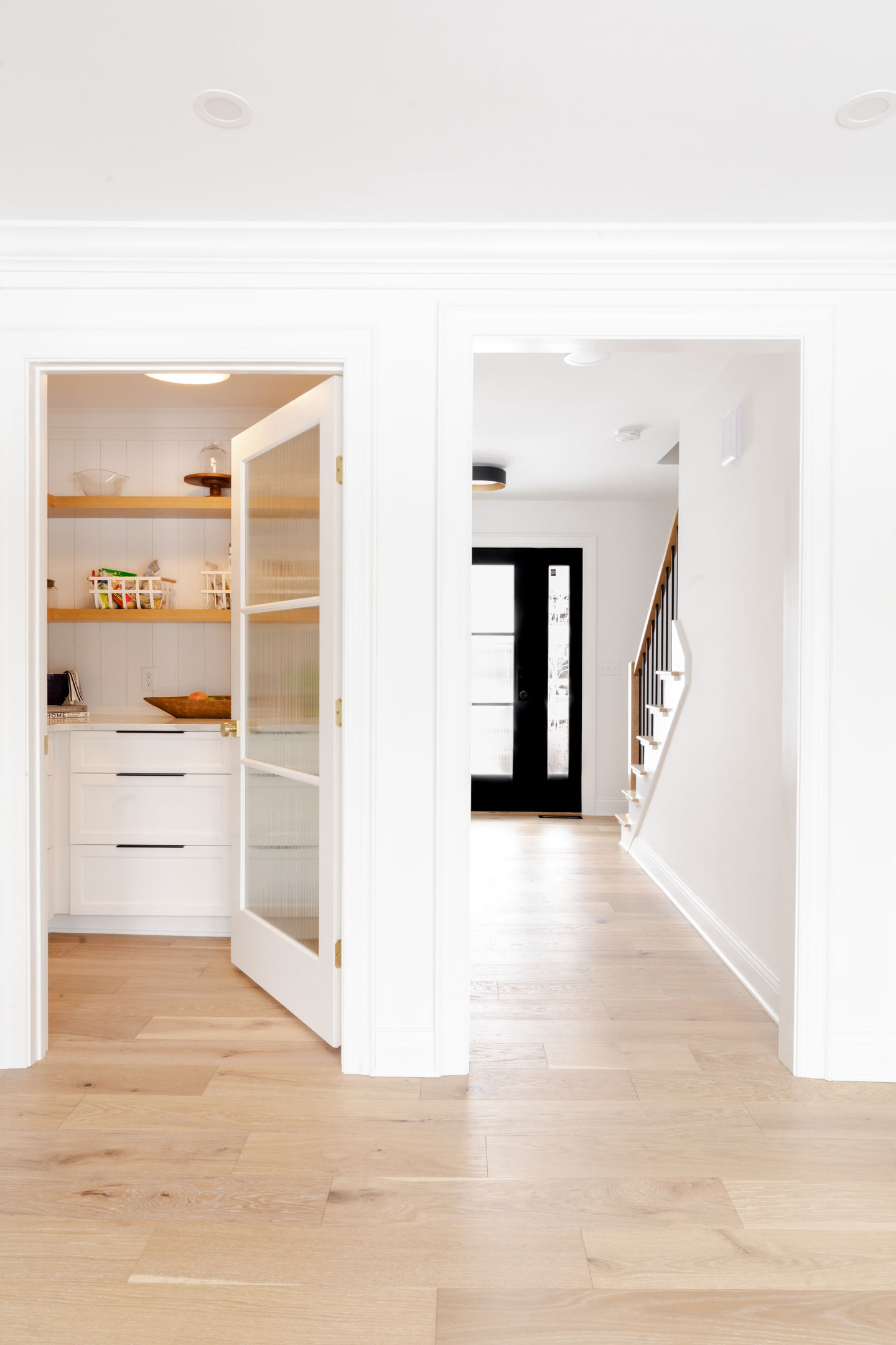 Edina Minnesota custom interior home remodel with walk in pantry featuring custom white oak shelving, painted white cabinets, reeded glass privacy door, white painted ceiling and walls, and black Andersen front door