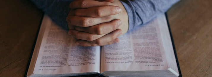 Hands Praying on top of open Bible