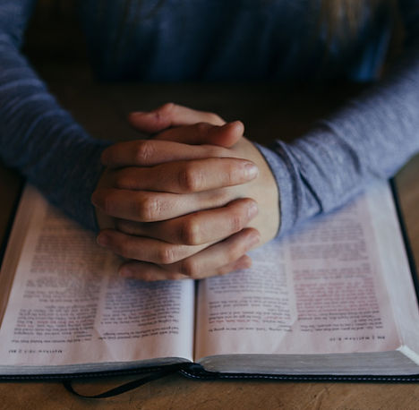 hands folded in prayer over an open bible