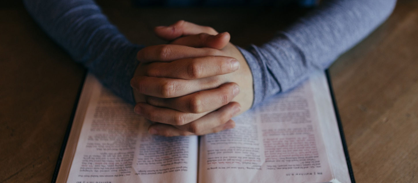 Person's hands clasped over an open bible, focused on reading. 
