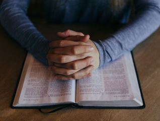 man's clasped hands on a Bible