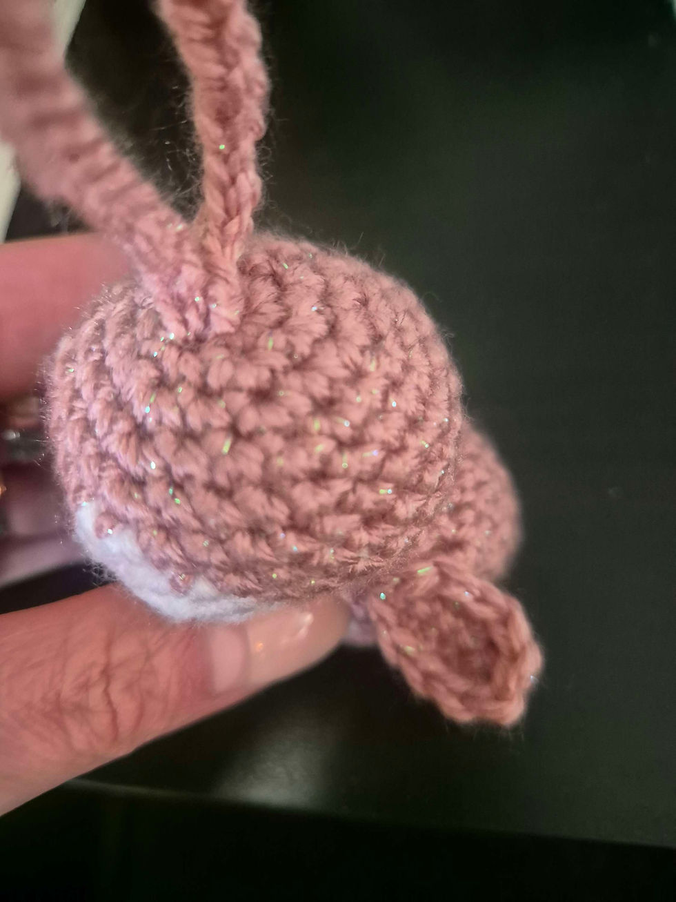 Gehäkeltes rosa Objekt mit Glitzerfäden, von einer Hand gehalten.