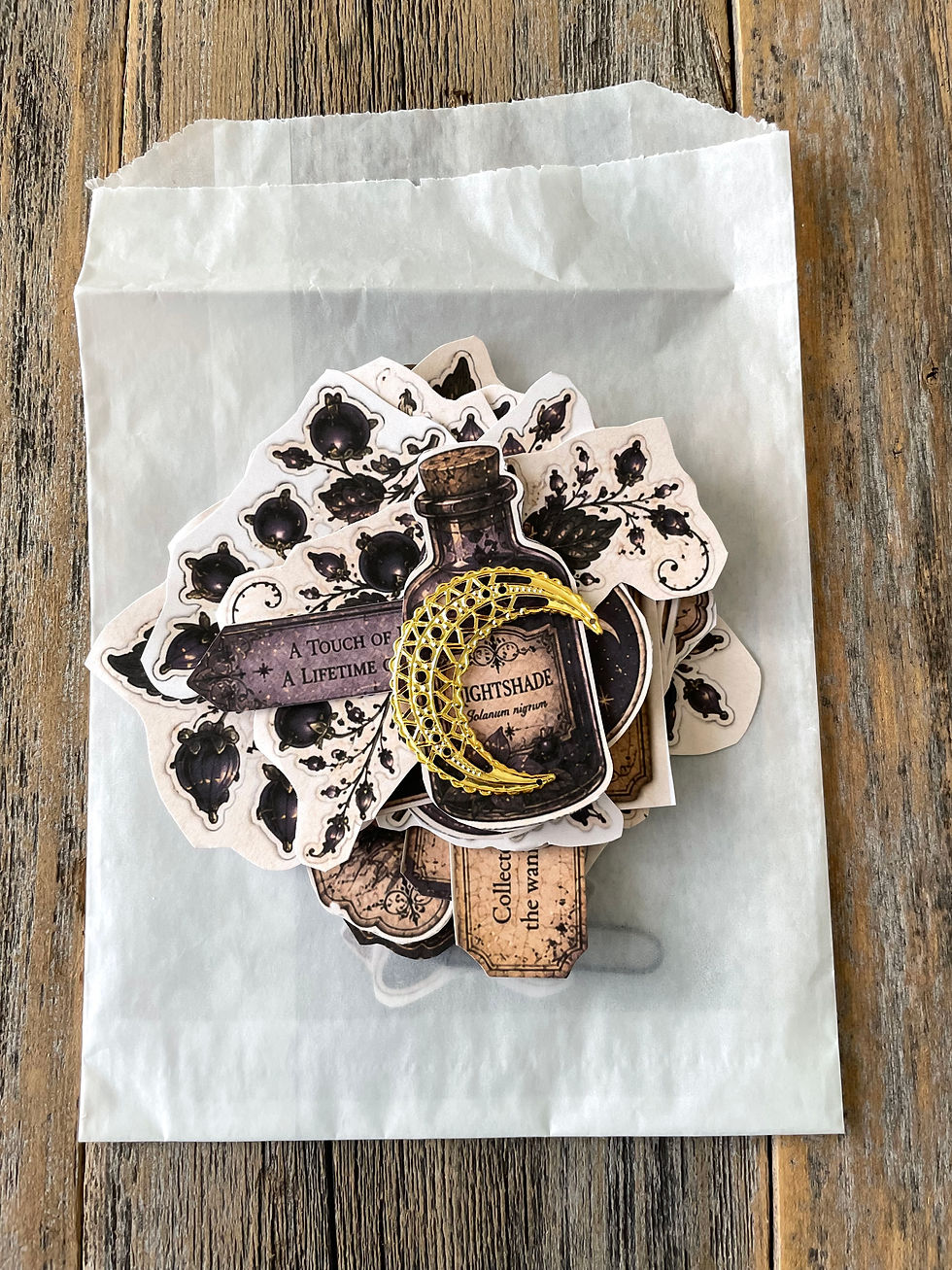 Thumbnail: Nightshade-themed paper embellishments arranged on a white glassine bag, including botanical cutouts, moonlit castle art, mag