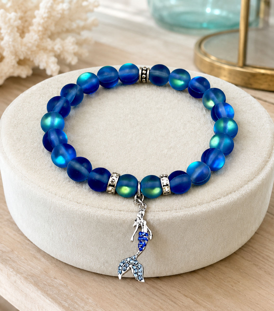 Cobalt-blue mermaid bracelet displayed on an ivory cushion in a coastal boutique setting.