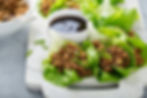 Lettuce wraps filled with seasoned ground meat and served with a dipping sauce.