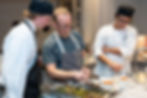 Chef instructing two culinary students on plating techniques.