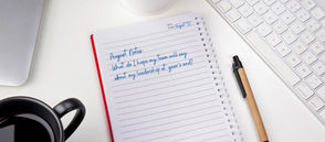 Open notebook with "August Notes: What do I hope my team will say about my leadership at year's end?" written. Pen and keyboard nearby.