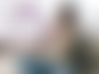 A woman is sitting on a couch wearing a worried facial expression and clutches a pillow.