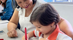Niño pequeño dibujando junto a su abuela en un aula del preescolar ABCnMe en Costa del Este, Panamá, ambos sonriendo y compartiendo un momento de conexión y aprendizaje.