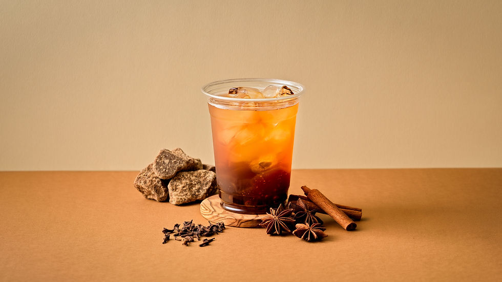 透明なプラスチックカップに入ったアイスティー。背景はベージュの壁とテーブル。周囲にシナモンスティックとスターアニスが配置されている。