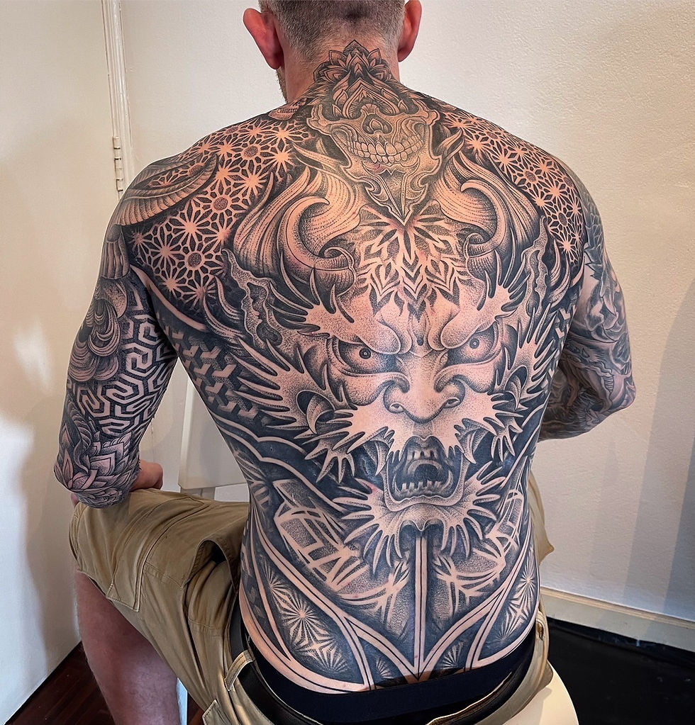 Man with a full back tattoo featuring a large dragon and tribal designs.