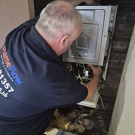 Stevie working on an open boiler inside a cupboard, wearing his FlameFlow polo shirt.