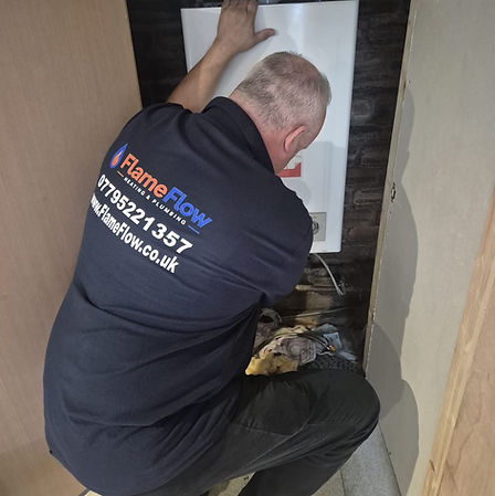 Stevie handling the front cover of a wall-mounted boiler in his FlameFlow uniform.