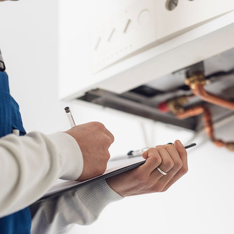 Technician inspecting a boiler, writing notes during annual boiler service safety check.