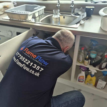 Stevie working beneath a kitchen sink in his FlameFlow uniform.