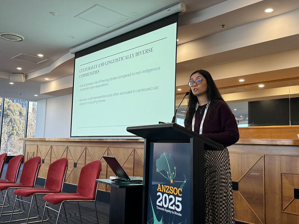 Sabine Allida delivers a presentation about Culturally and Linguistically Diverse Communities from the podium in a well-lit conference room. The screen beside her displays practical tools and strategies for research, and several empty red chairs are visible in the foreground.