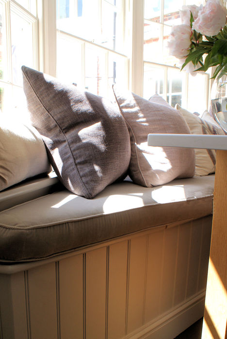 Custom bay window seat with a tongue and groove front panel, with upholstered seat cushion and throw cushions in tonal natural linen fabrics.